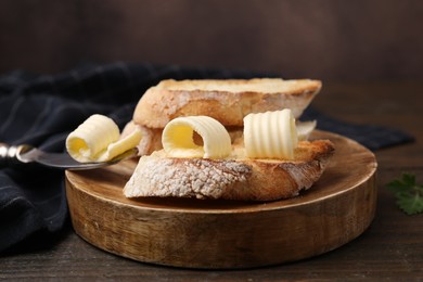 Photo of Tasty butter curls, knife and slices of bread on wooden table, closeup