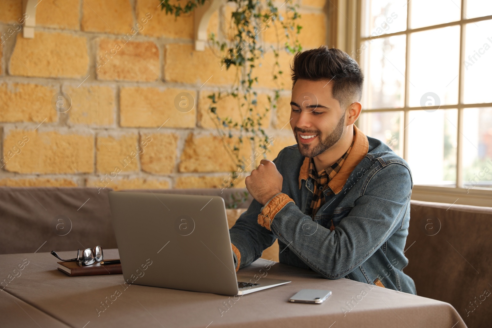 Photo of Young blogger working with laptop at table in cafe