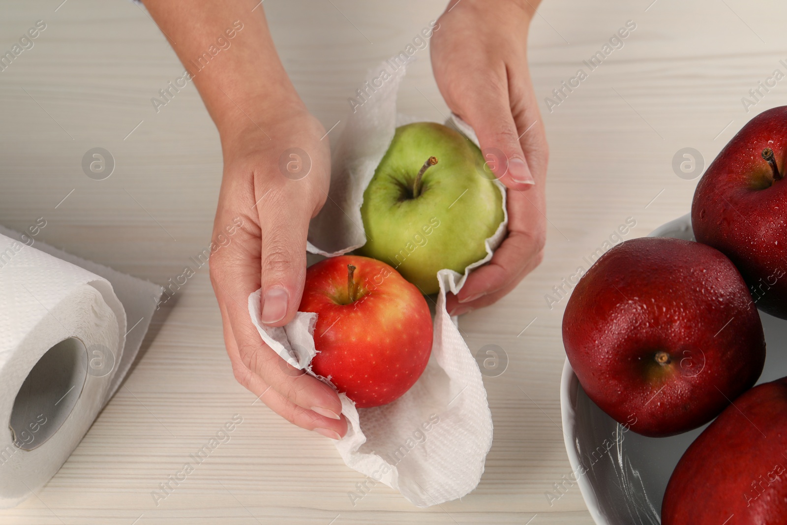 Photo of Woman wiping apples with paper towel at light wooden table, top view