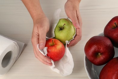 Woman wiping apples with paper towel at light wooden table, top view