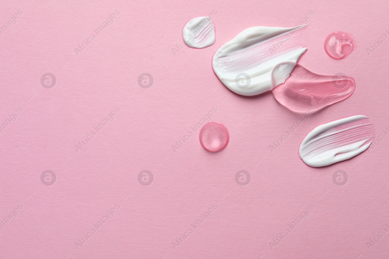 Photo of Samples of transparent gel and white cream on pink background, flat lay. Space for text