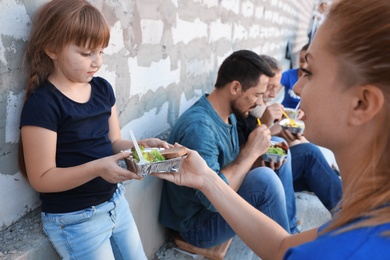 Poor people receiving food from volunteers near wall outdoors