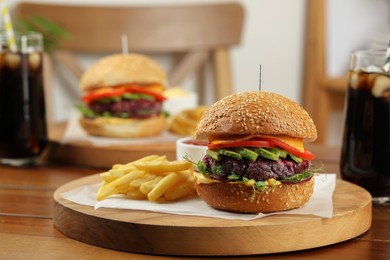 Tasty vegetarian burgers served with french fries and soda drinks on wooden table, space for text