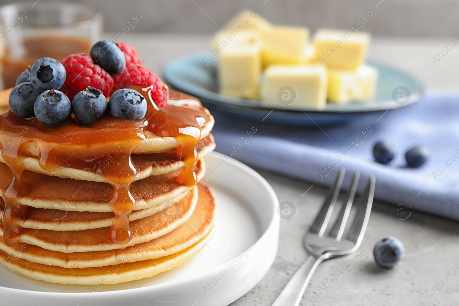 Photo of Delicious pancakes with fresh berries and syrup on grey table, closeup