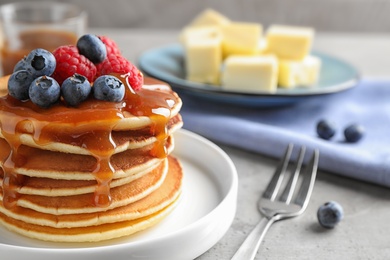 Delicious pancakes with fresh berries and syrup on grey table, closeup