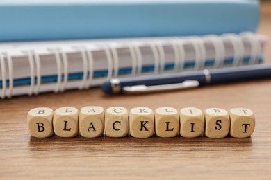 Photo of Cubes with word Blacklist and office stationery on wooden desk, closeup