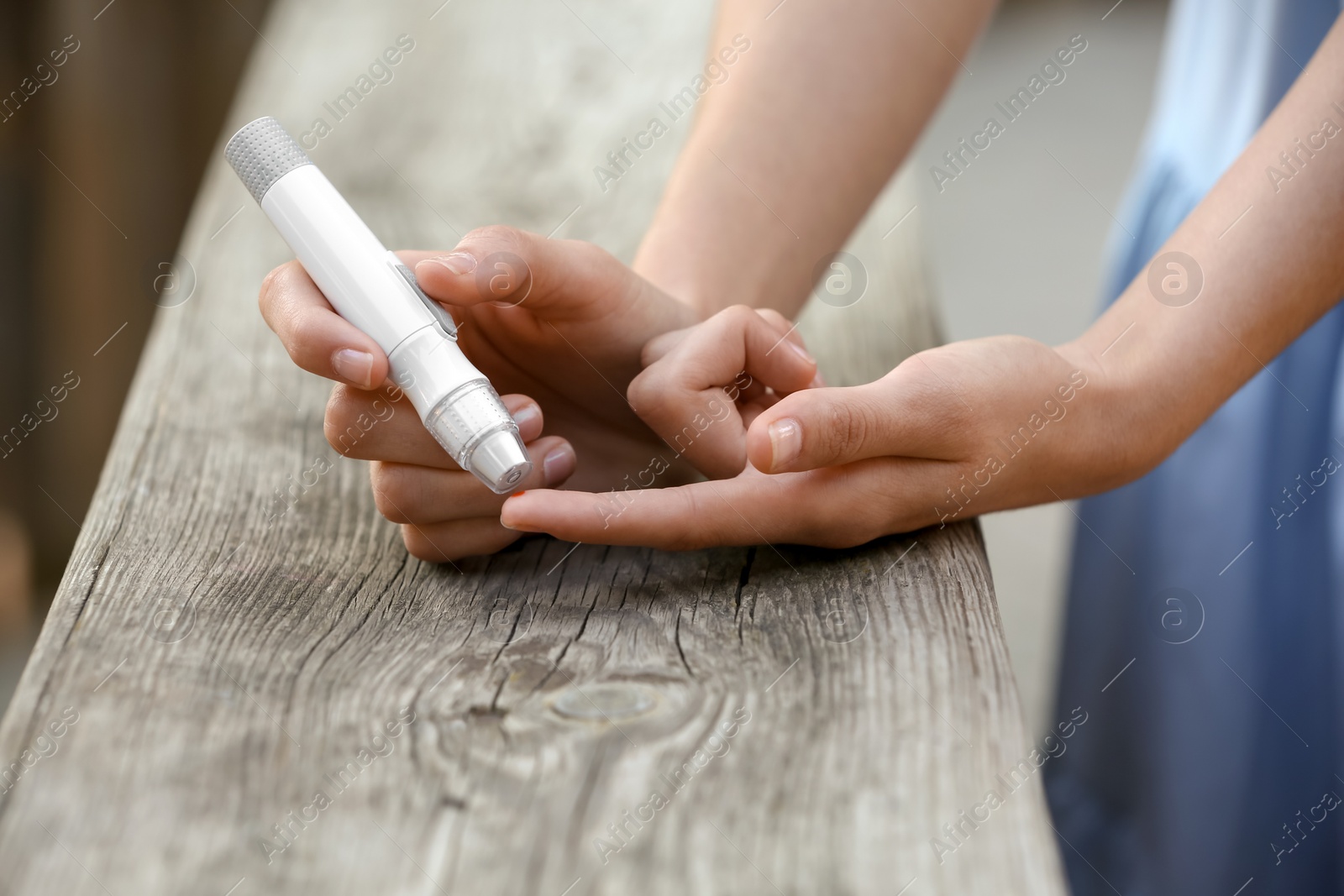 Photo of Woman using lancet pen near wooden surface outdoors. Diabetes control