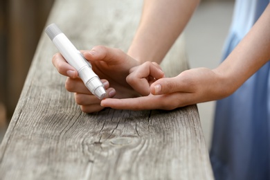 Woman using lancet pen near wooden surface outdoors. Diabetes control