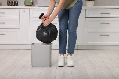 Photo of Woman taking garbage bag out of trash bin in kitchen, closeup