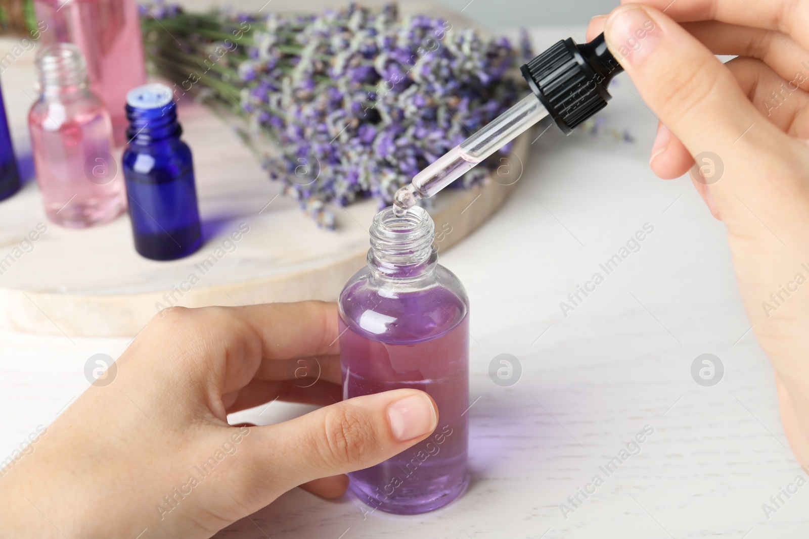 Photo of Woman with bottle of lavender essential oil at white wooden table, closeup