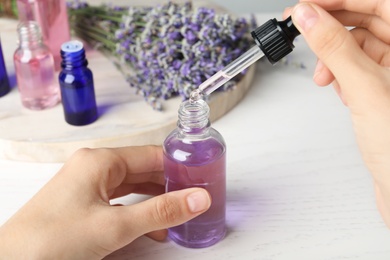 Photo of Woman with bottle of lavender essential oil at white wooden table, closeup