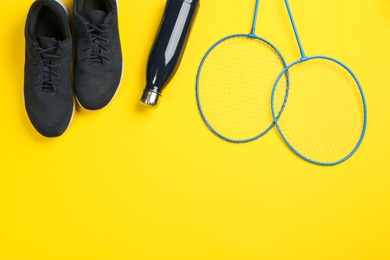 Rackets, sneakers and bottle on yellow background, flat lay with space for text. Playing badminton