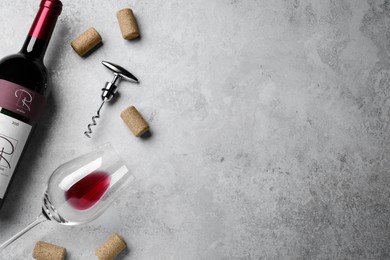 Photo of Corkscrew with wine bottle, glass and stoppers on light grey stone table, flat lay. Space for text