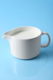 Jug of fresh milk on light blue background