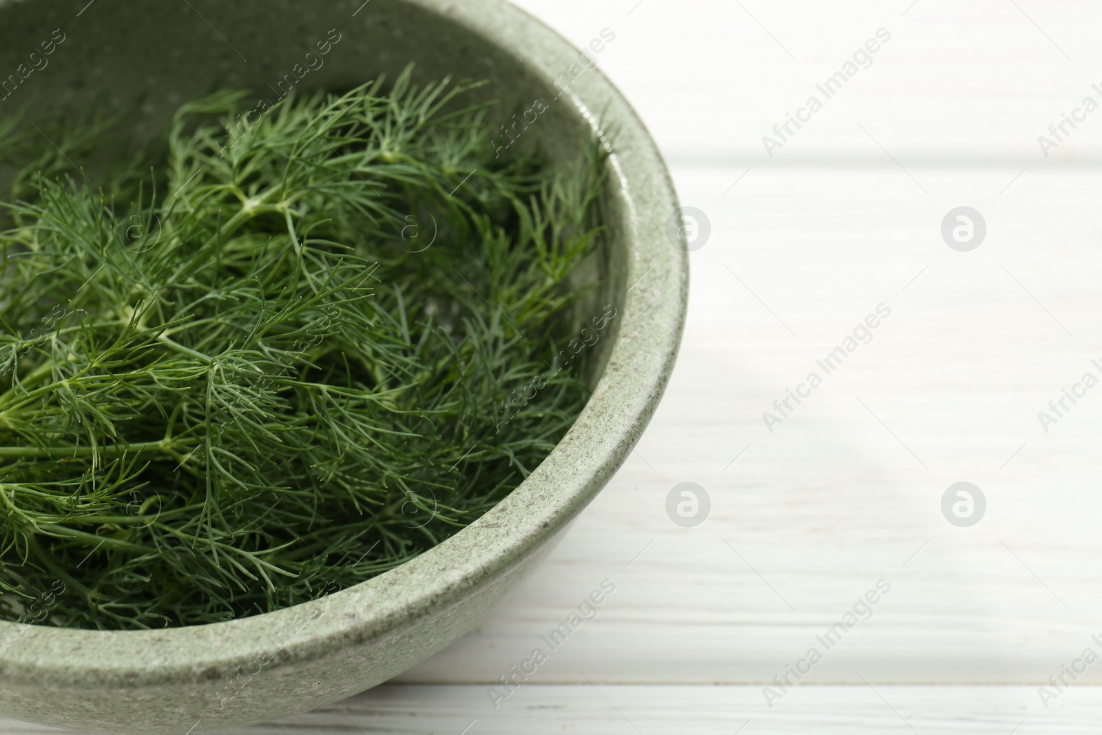 Photo of Bowl of fresh green dill on white wooden table, closeup. Space for text