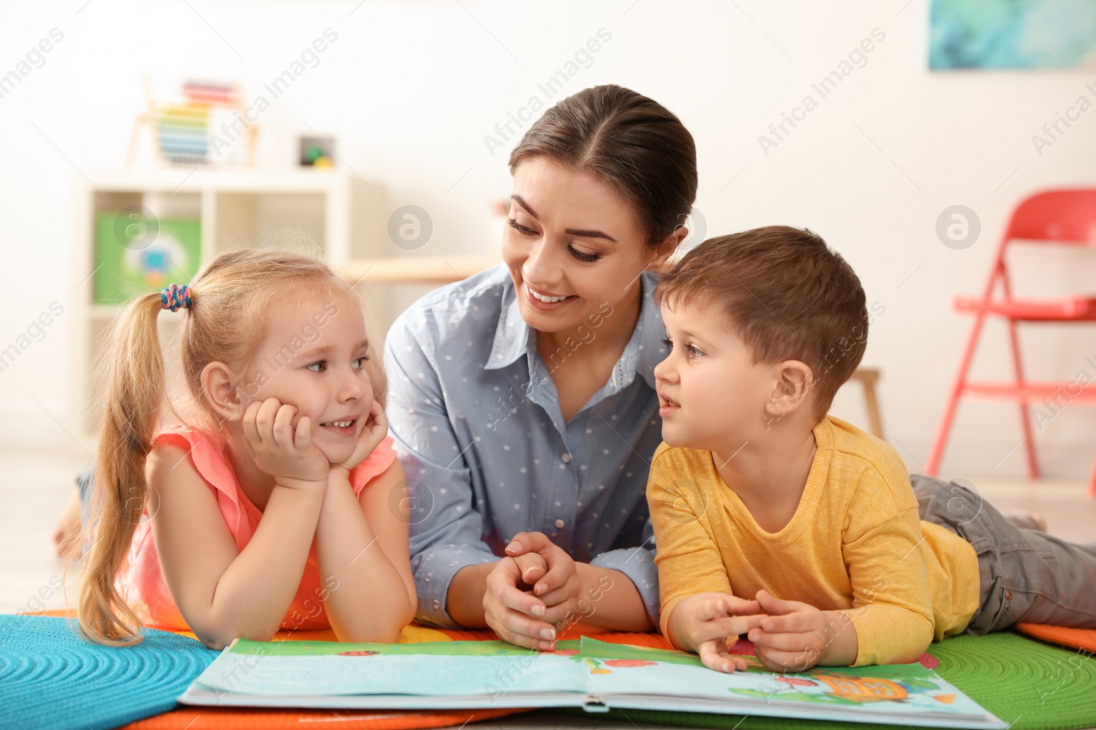 Photo of Kindergarten teacher reading book to children indoors. Learning and playing