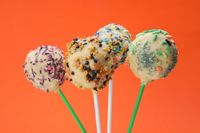 Photo of Sweet cake pops decorated with sprinkles on orange background, closeup. Delicious confectionery