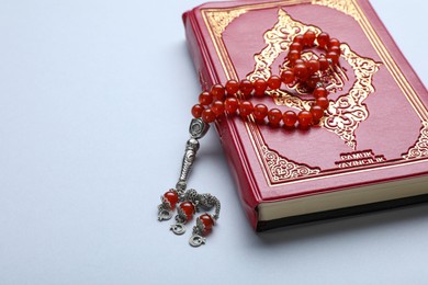 Photo of Muslim prayer beads and Quran on light background, closeup. Space for text