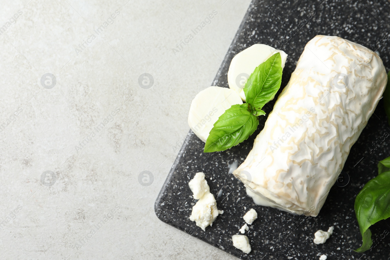 Photo of Delicious fresh goat cheese with basil on light grey table, top view. Space for text