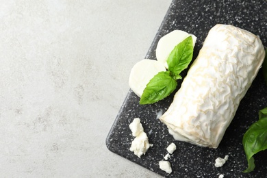 Photo of Delicious fresh goat cheese with basil on light grey table, top view. Space for text