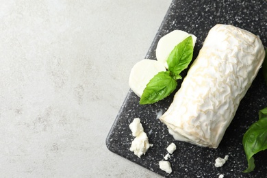 Delicious fresh goat cheese with basil on light grey table, top view. Space for text