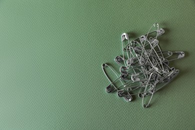 Photo of Pile of safety pins on green background, flat lay. Space for text