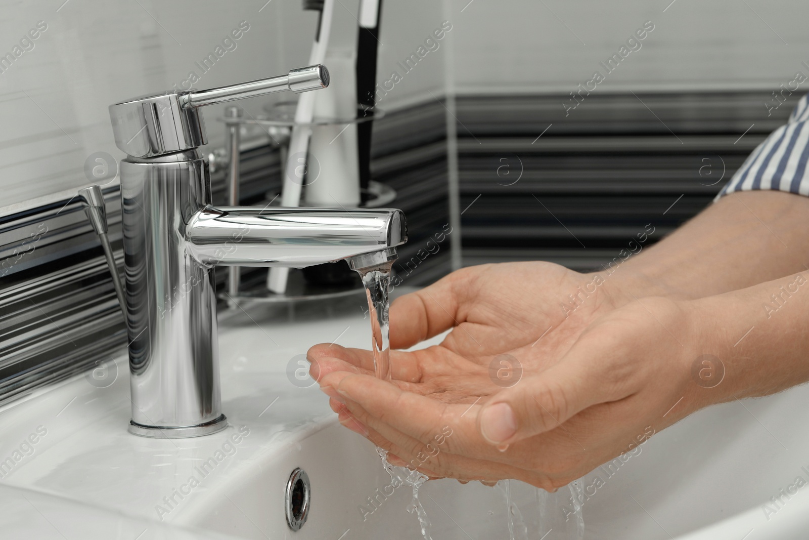 Photo of Man using water tap to wash hands in bathroom, closeup