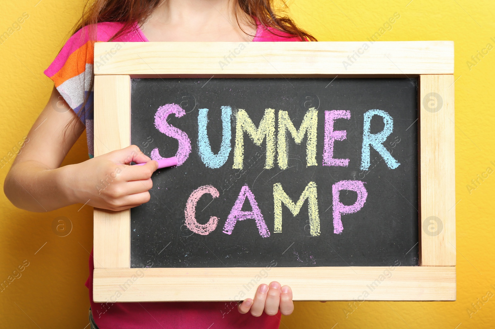 Photo of Girl writing SUMMER CAMP with colorful chalk on blackboard, closeup