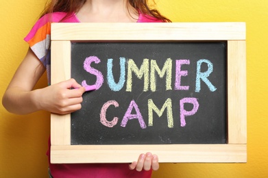 Photo of Girl writing SUMMER CAMP with colorful chalk on blackboard, closeup