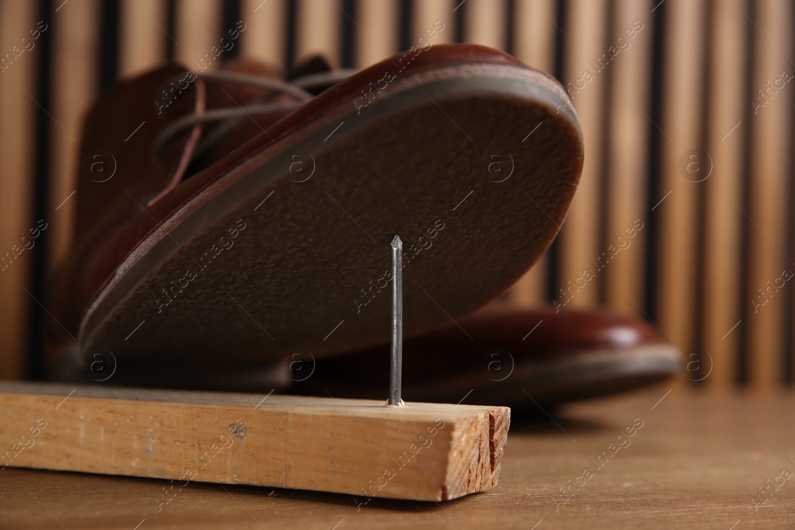 Photo of Metal nail in wooden plank and shoes on table, closeup