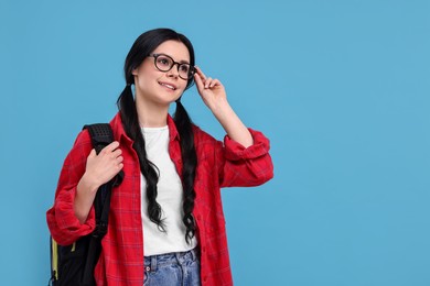 Photo of Smiling student in glasses with backpack on light blue background. Space for text