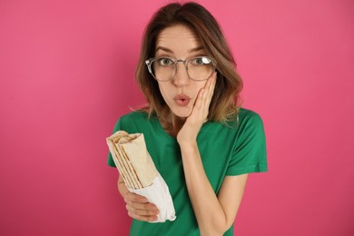 Emotional young woman with delicious shawarma on pink background