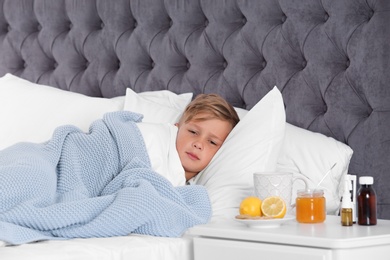 Photo of Ill boy suffering from cold in bed and cough remedies on bedside table