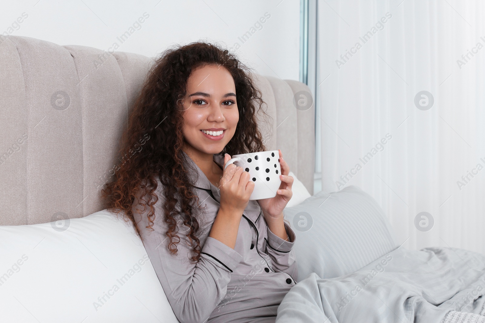 Photo of Beautiful African American woman with cup of drink in bed at home