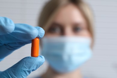 Doctor holding pill on light background, selective focus. Space for text