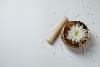 Photo of Tibetan singing bowl with water, beautiful chrysanthemum flower and mallet on white background, top view. Space for text