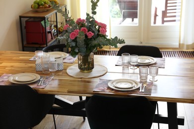 Photo of Beautiful table setting with bouquet indoors. Roses and eucalyptus branches in vase