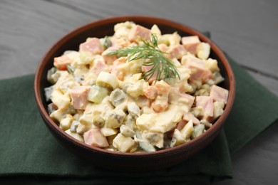 Photo of Tasty Olivier salad with boiled sausage in bowl on grey table, closeup