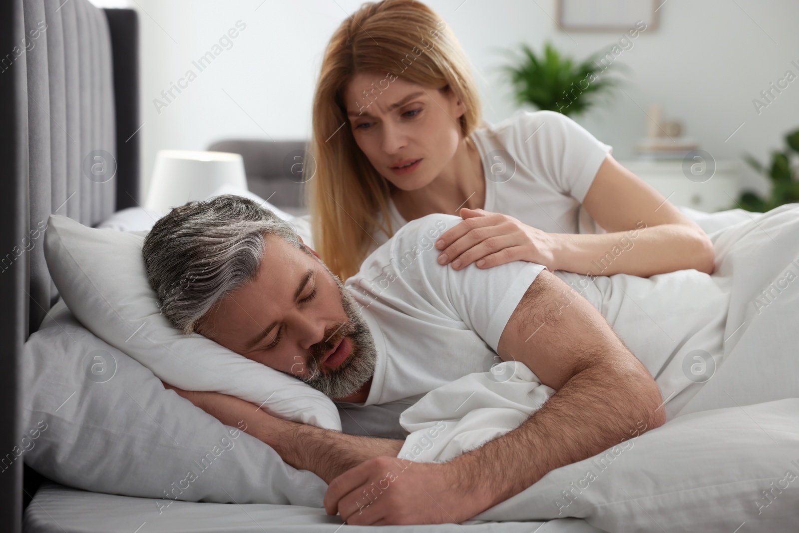Photo of Irritated woman waking up her snoring husband in bed at home