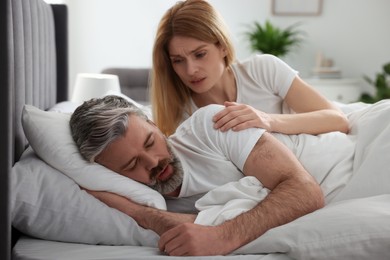 Photo of Irritated woman waking up her snoring husband in bed at home