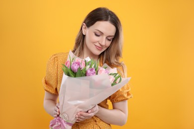 Photo of Happy young woman with bouquet of beautiful tulips on yellow background