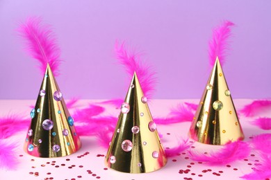 Photo of Golden party hats with bright feathers, rhinestones and confetti on color background