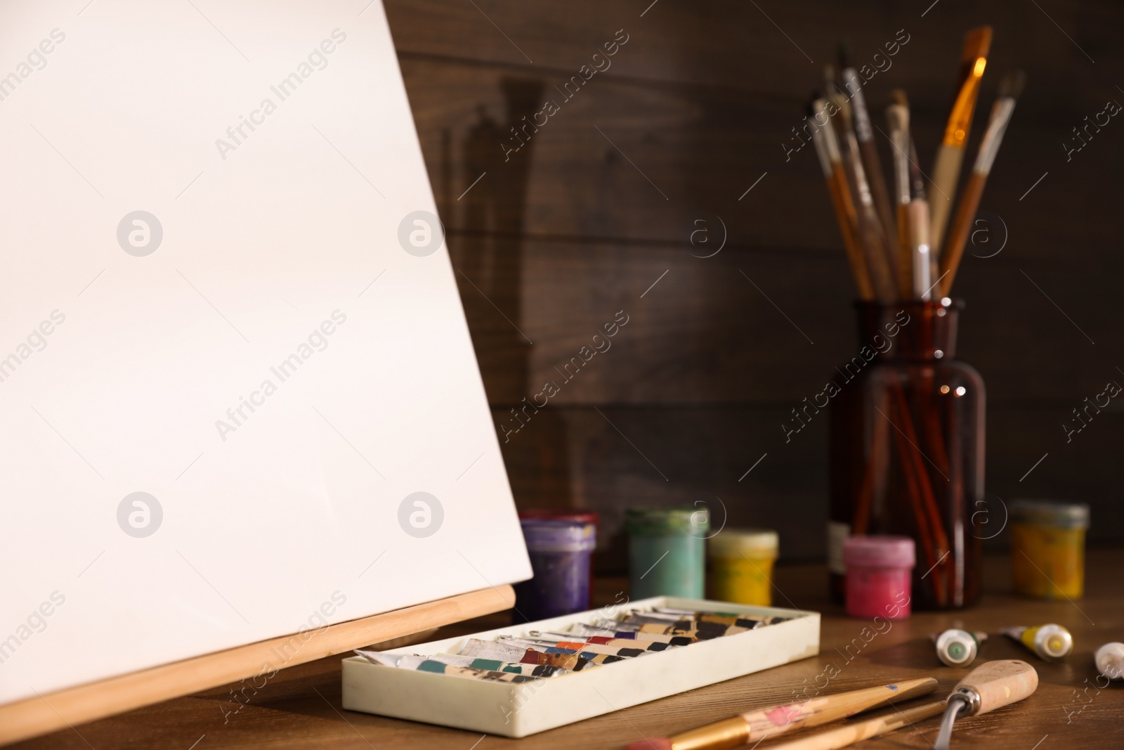 Photo of Easel with canvas and art supplies on wooden table