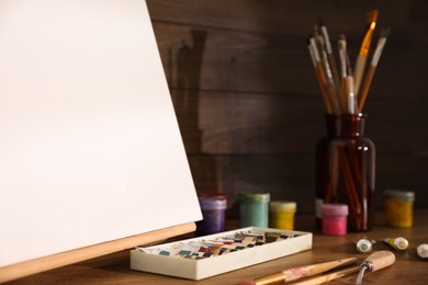 Photo of Easel with canvas and art supplies on wooden table