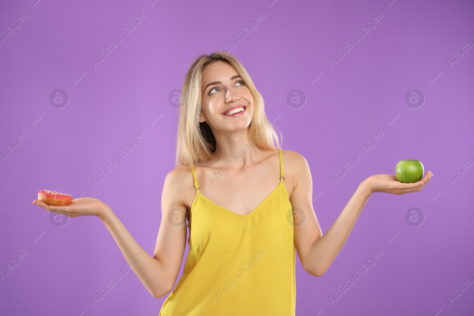 Photo of Woman choosing between doughnut and healthy apple on violet background