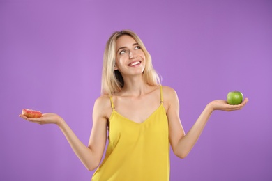 Woman choosing between doughnut and healthy apple on violet background