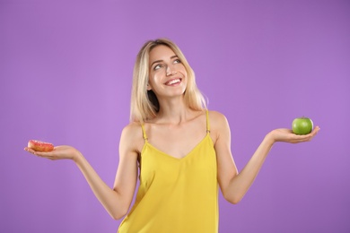 Photo of Woman choosing between doughnut and healthy apple on violet background