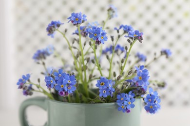 Beautiful blue forget-me-not flowers in cup against blurred background, closeup