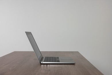 Photo of New modern laptop on empty wooden table indoors