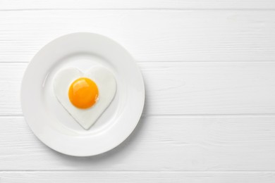 Romantic breakfast with heart shaped fried egg on white wooden table, top view. Space for text